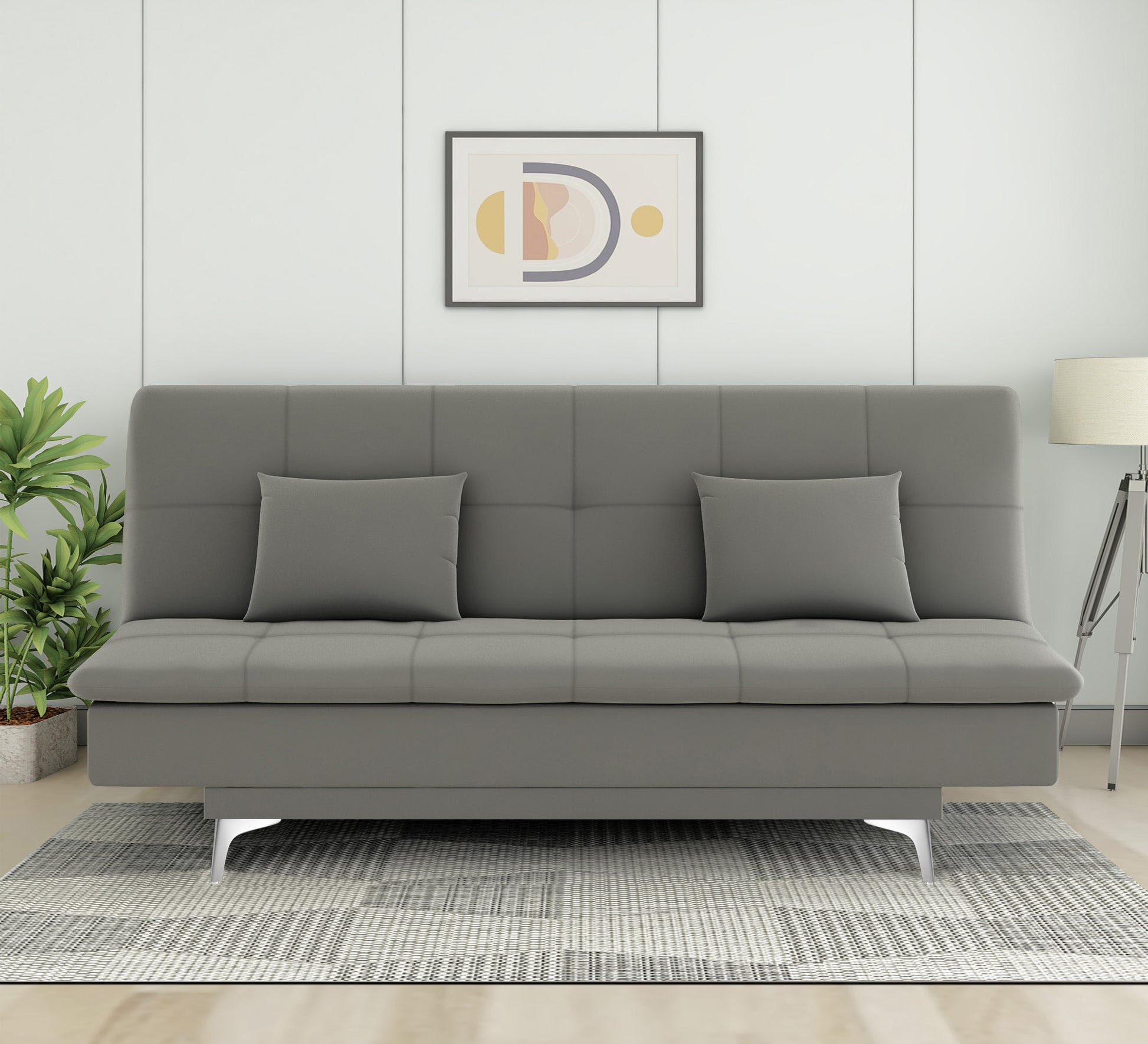 A gray velvet suede 3-seater sofa cum bed with two additional cushions, placed in a room with a light gray wall, a decorative picture on the wall, and a white lamp on a side table.